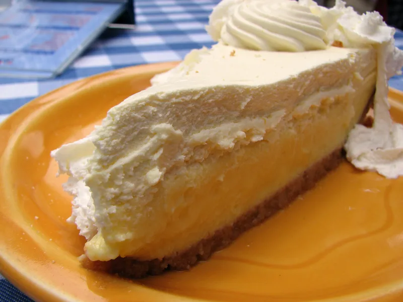 A slice of key lime pie with a graham cracker crust and whipped cream on a yellow plate