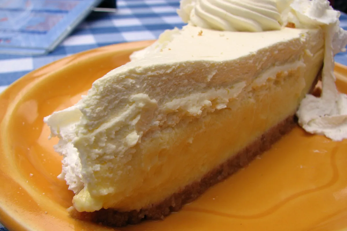 A slice of key lime pie with a graham cracker crust and whipped cream on a yellow plate