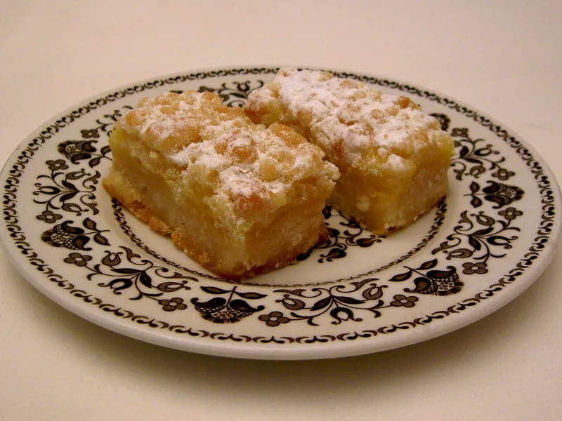 Two lemon bars dusted with powdered sugar on a patterned plate