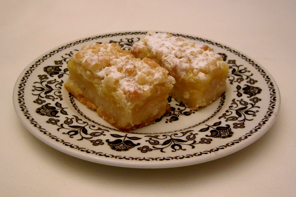 Two lemon bars dusted with powdered sugar on a patterned plate