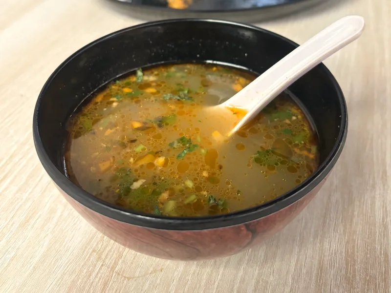 A black bowl of warm chicken soup with herbs and vegetables