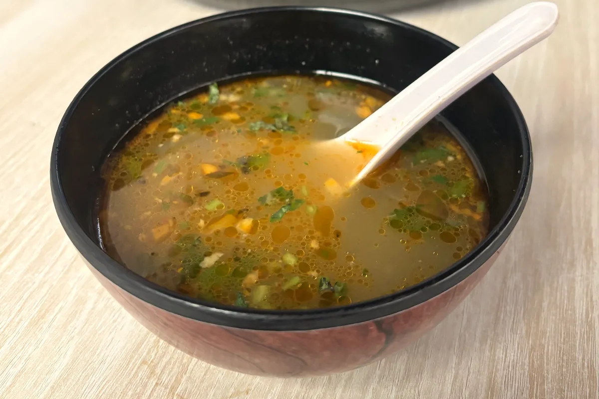 A black bowl of warm chicken soup with herbs and vegetables