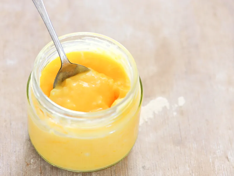 Open jar of homemade lemon curd with a spoon lifting a thick, glossy spoonful