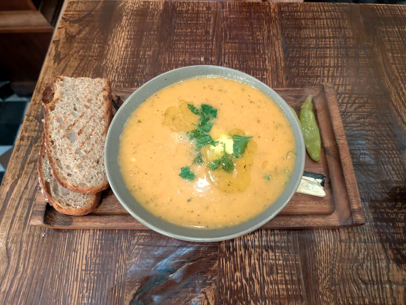 A bowl of smooth golden lentil soup topped with fresh herbs and olive oil, with slices of crusty bread alongside on a wooden board
