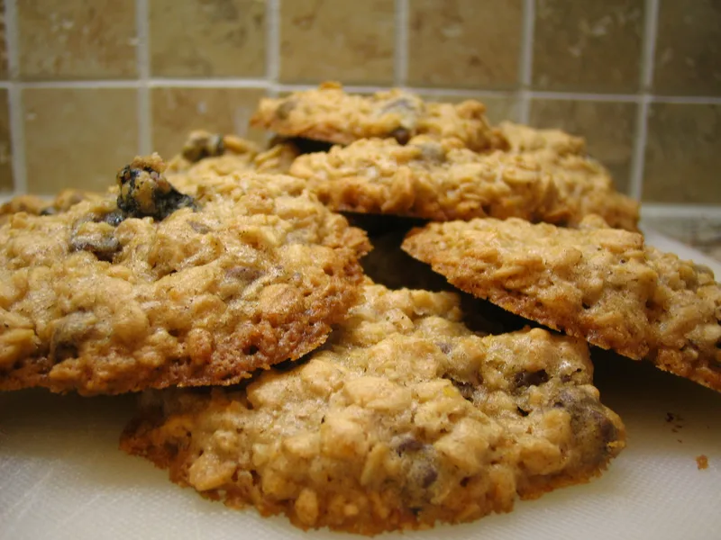 A stack of golden oatmeal cookies with raisins and chocolate chips on a white surface