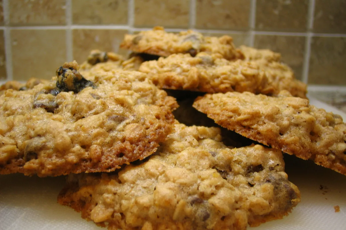 A stack of golden oatmeal cookies with raisins and chocolate chips on a white surface