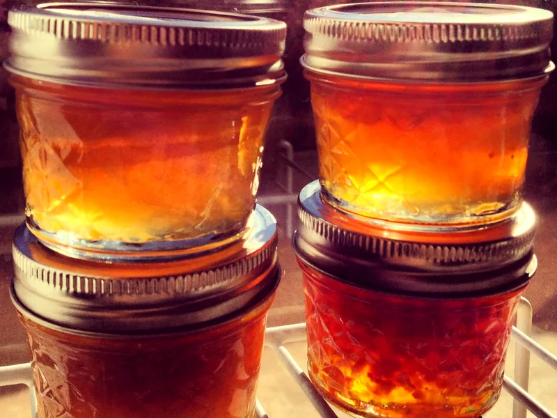 Four small sealed jars of golden-orange marmalade stacked on a rack, glowing amber in the light