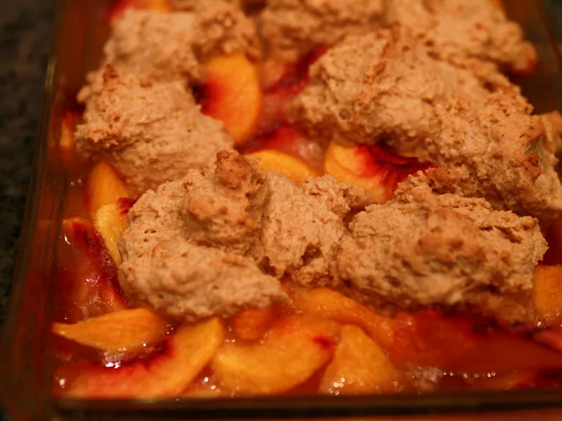 Easy peach cobbler in a glass baking dish with golden biscuit topping and juicy peach slices bubbling at the edges