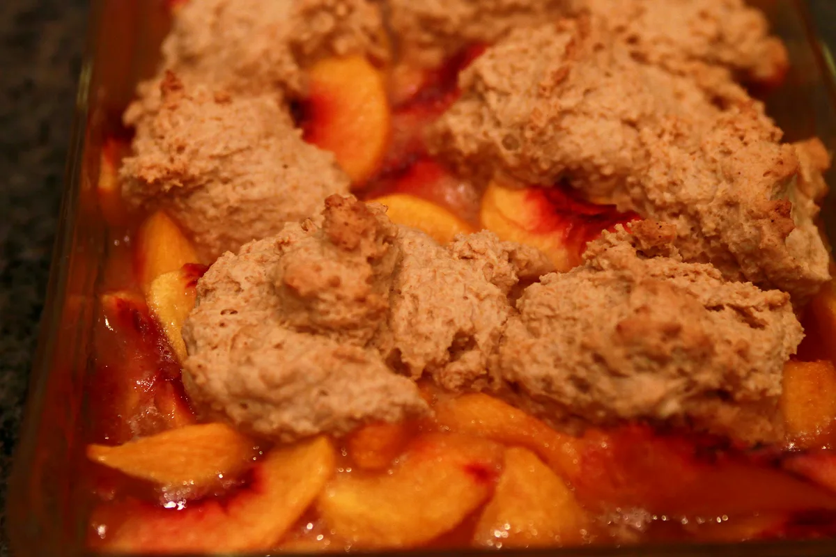 Easy peach cobbler in a glass baking dish with golden biscuit topping and juicy peach slices bubbling at the edges