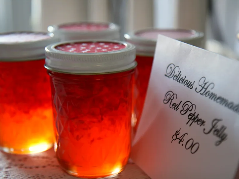 Mason jars of glowing scarlet red pepper jelly beside a handwritten tag that reads Red Pepper Jelly