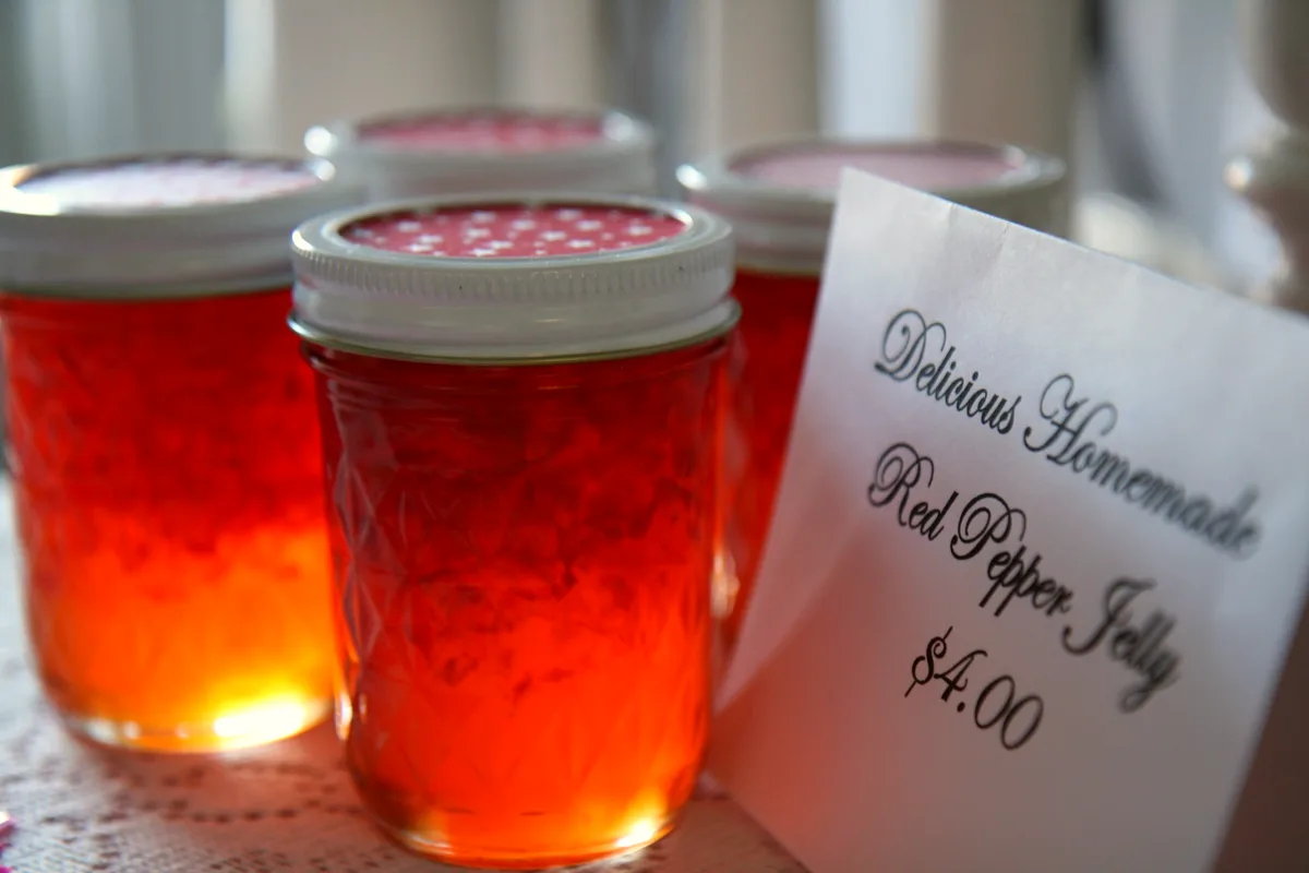 Mason jars of glowing scarlet red pepper jelly beside a handwritten tag that reads Red Pepper Jelly