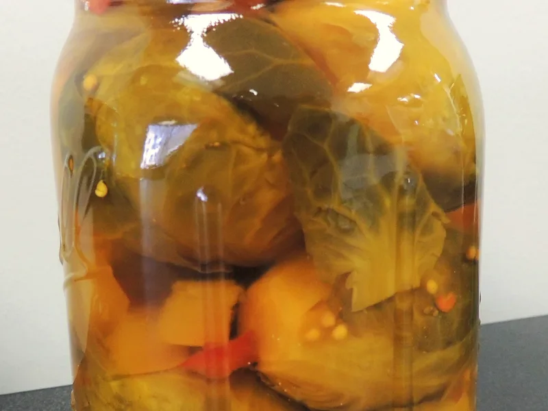 Mason jar of pickled Brussels sprouts in golden brine with mustard seeds and red pepper