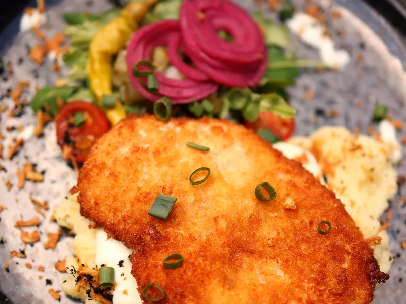 Crispy pork chop on mashed potatoes with fresh vegetables on a plate