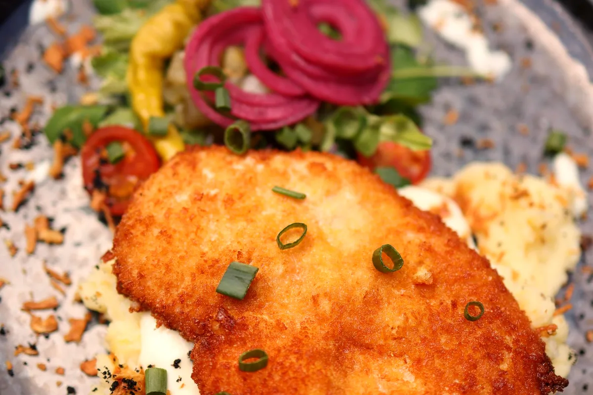 Crispy pork chop on mashed potatoes with fresh vegetables on a plate