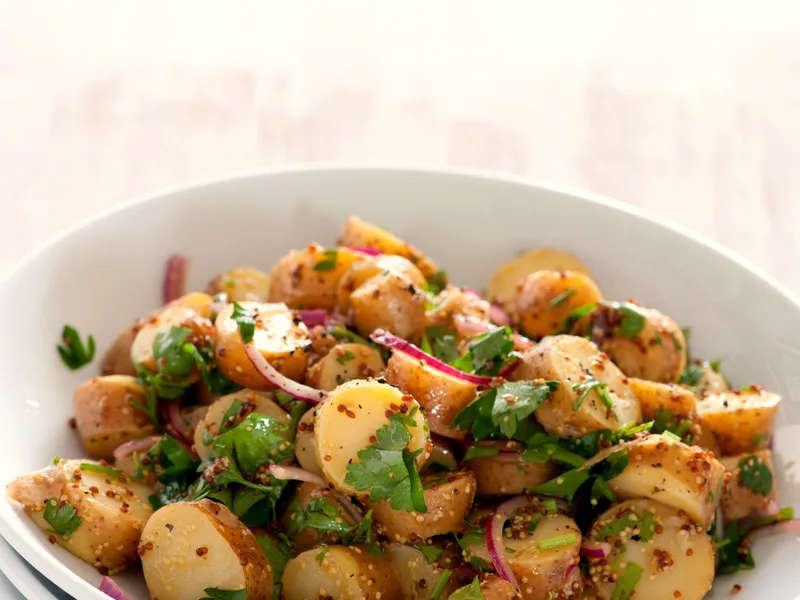 Bowl of sliced baby potatoes in wholegrain mustard vinaigrette with red onion slices and fresh parsley