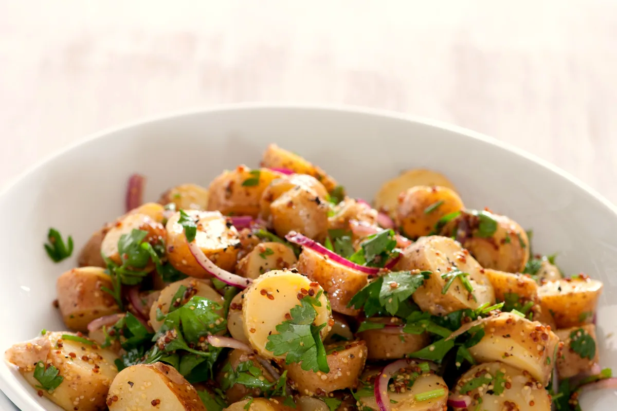 Bowl of sliced baby potatoes in wholegrain mustard vinaigrette with red onion slices and fresh parsley