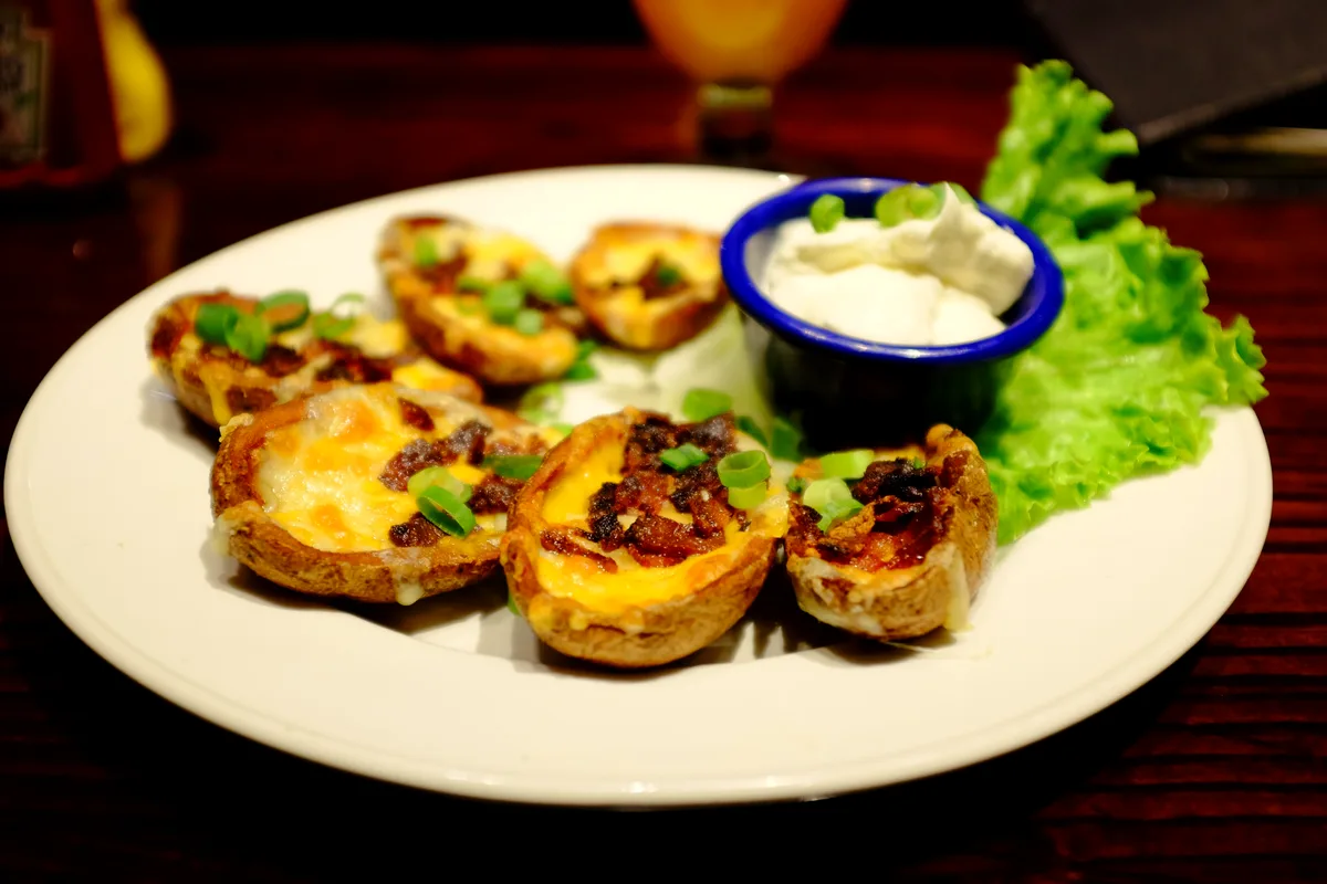 Crispy air fryer potato skins loaded with melted cheddar, bacon bits and scallions, with sour cream for dipping
