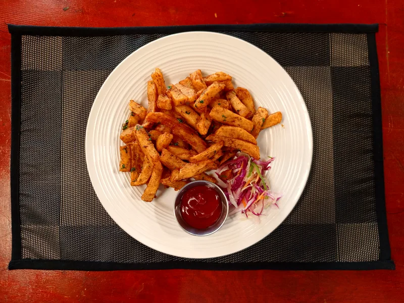 A plate of seasoned potato fries garnished with chopped herbs, served with coleslaw and tomato ketchup