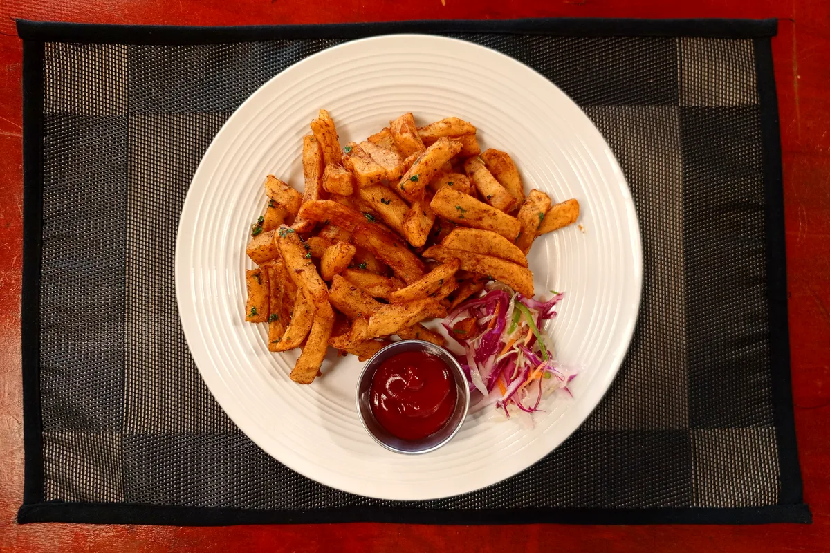 A plate of seasoned potato fries garnished with chopped herbs, served with coleslaw and tomato ketchup