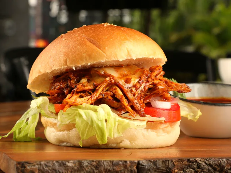 Slow cooker BBQ pulled chicken piled on a bun with coleslaw, with extra sauce in a small bowl