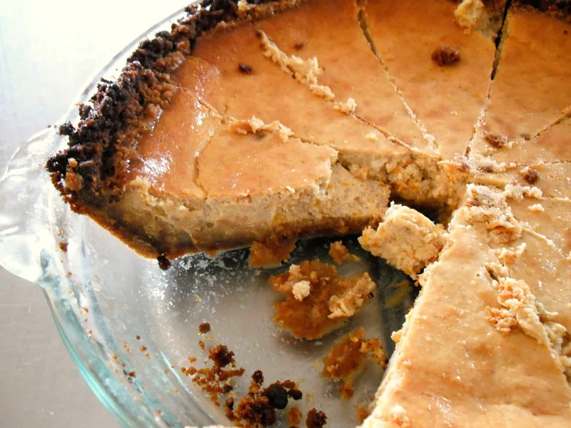 Sliced pumpkin cheesecake with a dark gingersnap crumb crust in a glass pie dish