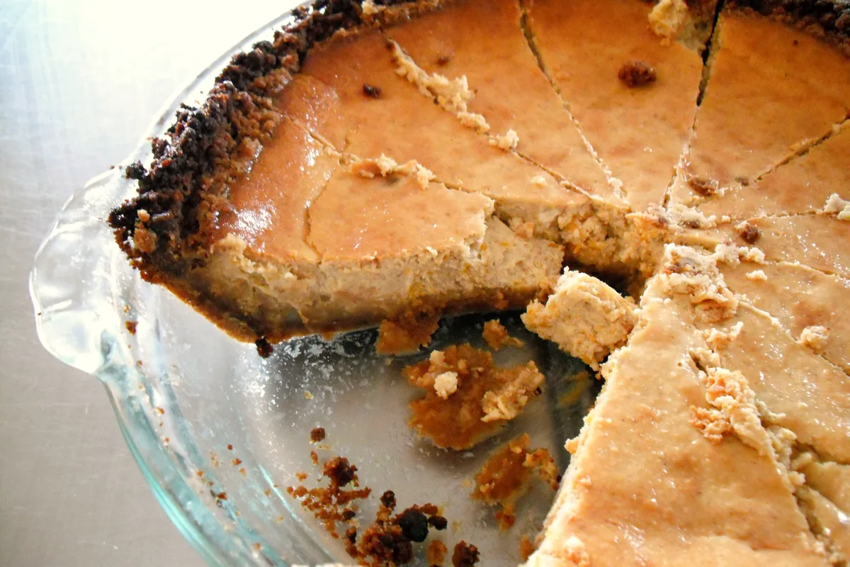Sliced pumpkin cheesecake with a dark gingersnap crumb crust in a glass pie dish