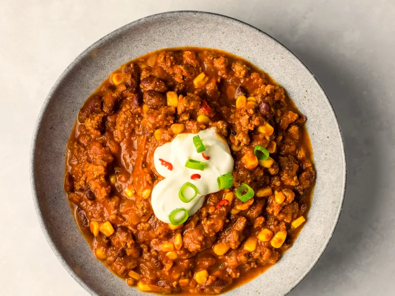 A bowl of chili with beans and corn topped with sour cream