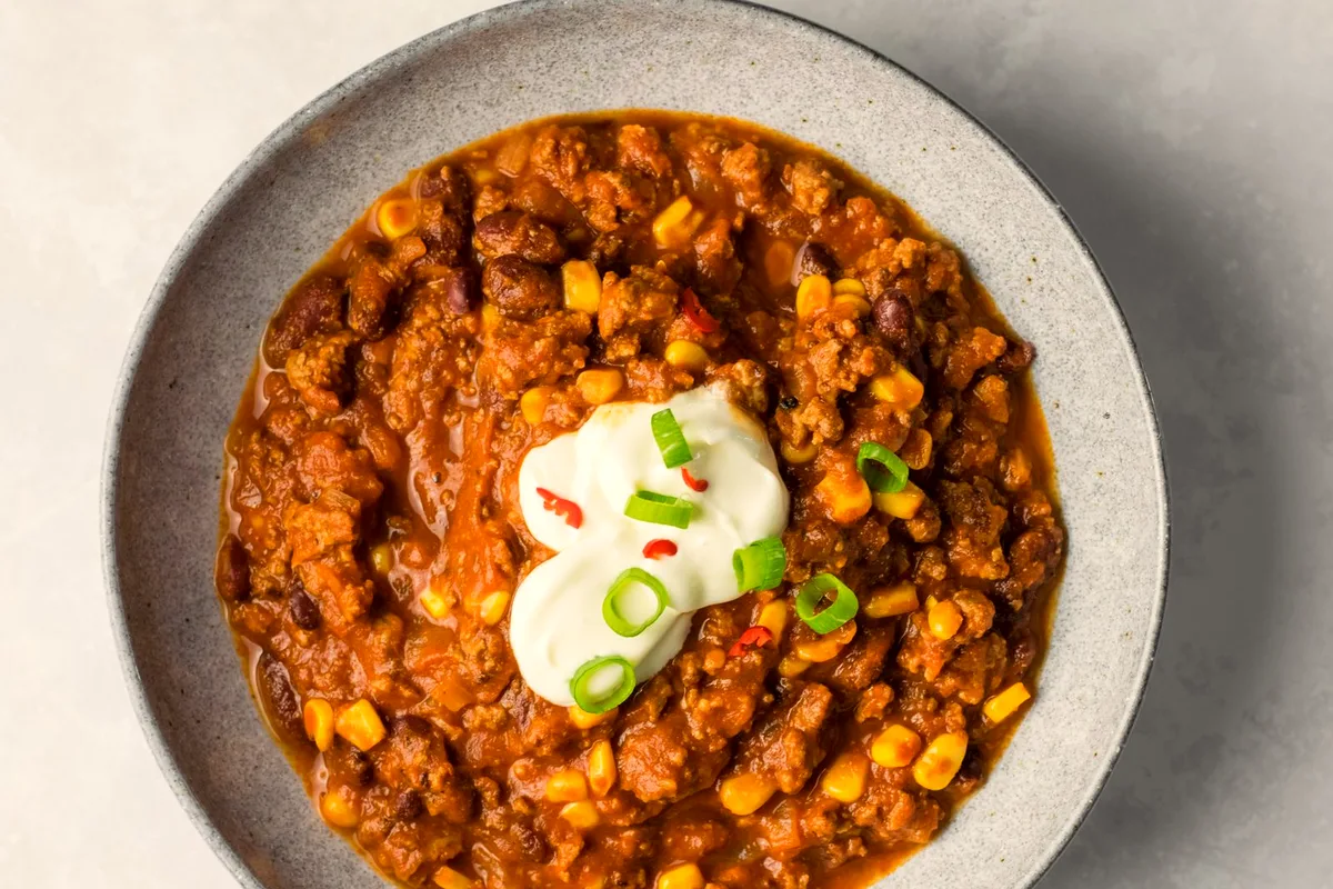 A bowl of chili with beans and corn topped with sour cream