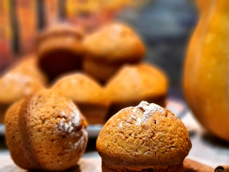 Golden-brown pumpkin cinnamon muffins dusted with powdered sugar, with a small pumpkin at the frame edge