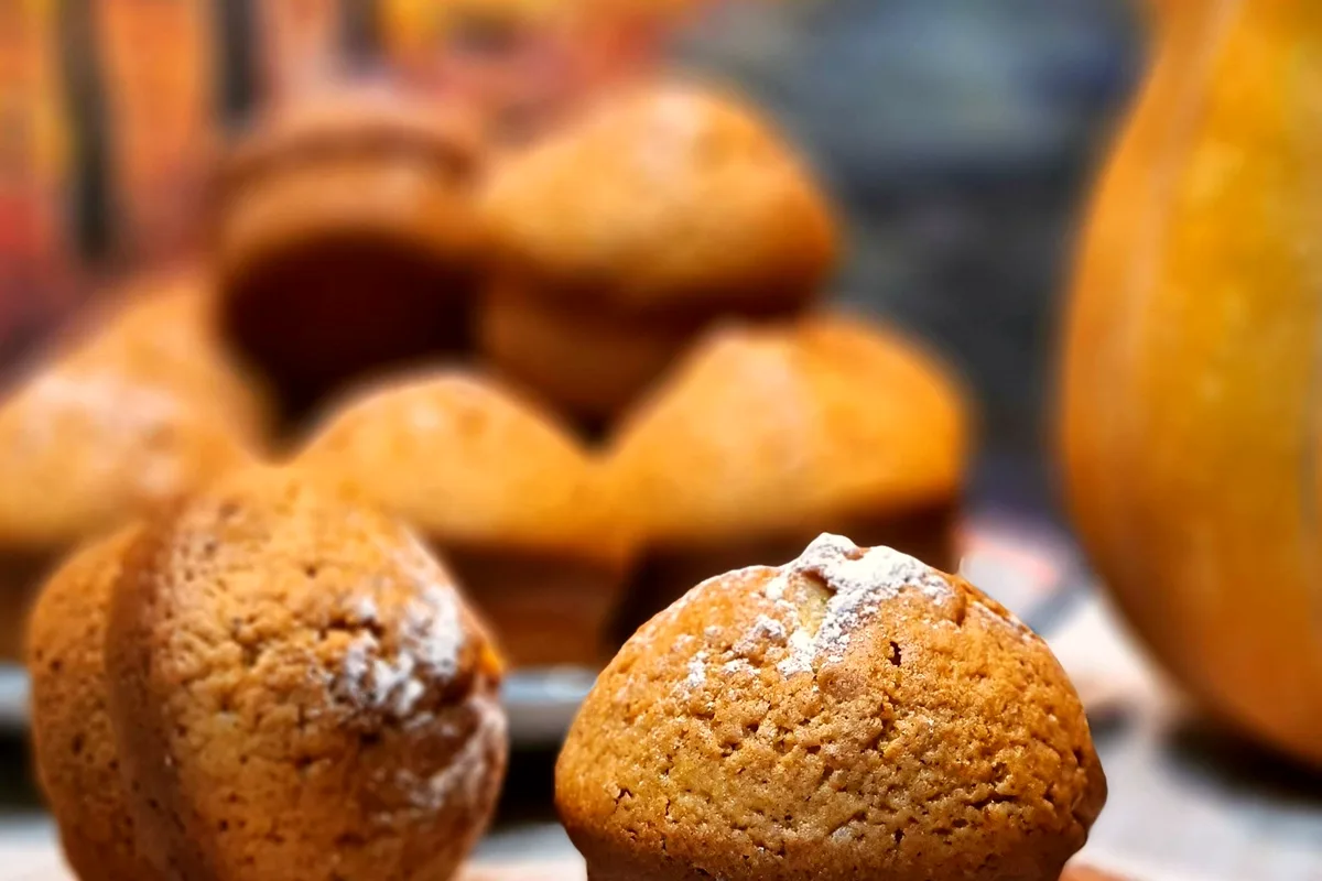 Golden-brown pumpkin cinnamon muffins dusted with powdered sugar, with a small pumpkin at the frame edge