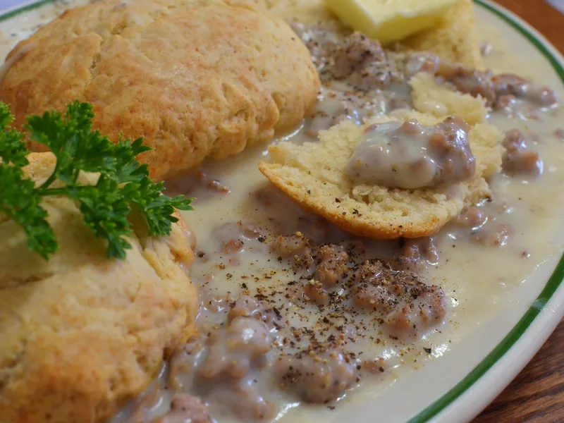 Plate of easy biscuits and sausage gravy with golden split biscuits covered in creamy peppered sausage gravy