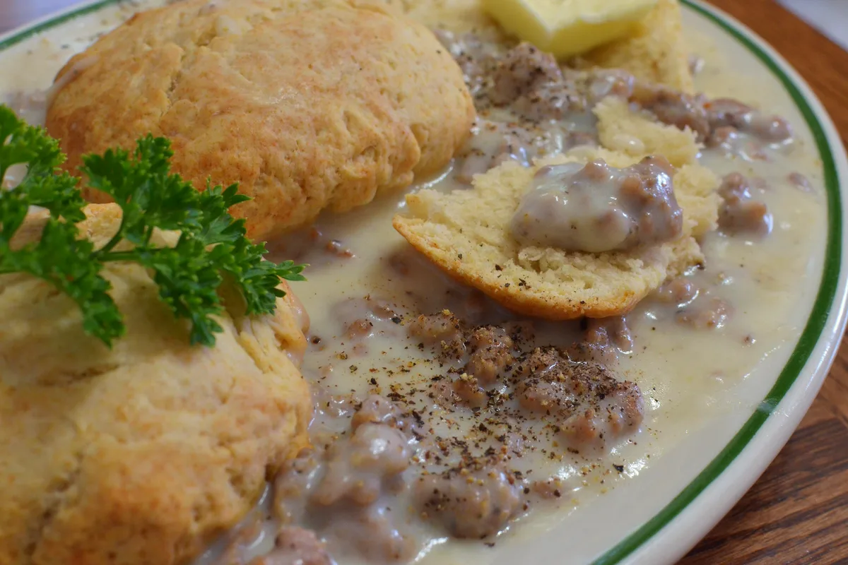 Plate of easy biscuits and sausage gravy with golden split biscuits covered in creamy peppered sausage gravy