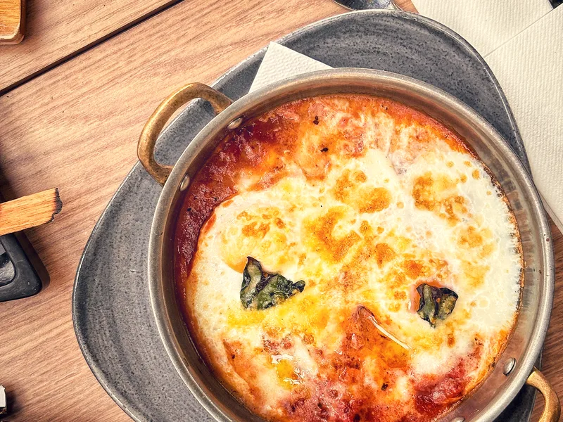 A bubbling dish of baked eggs in tomato sauce garnished with basil in a round pan