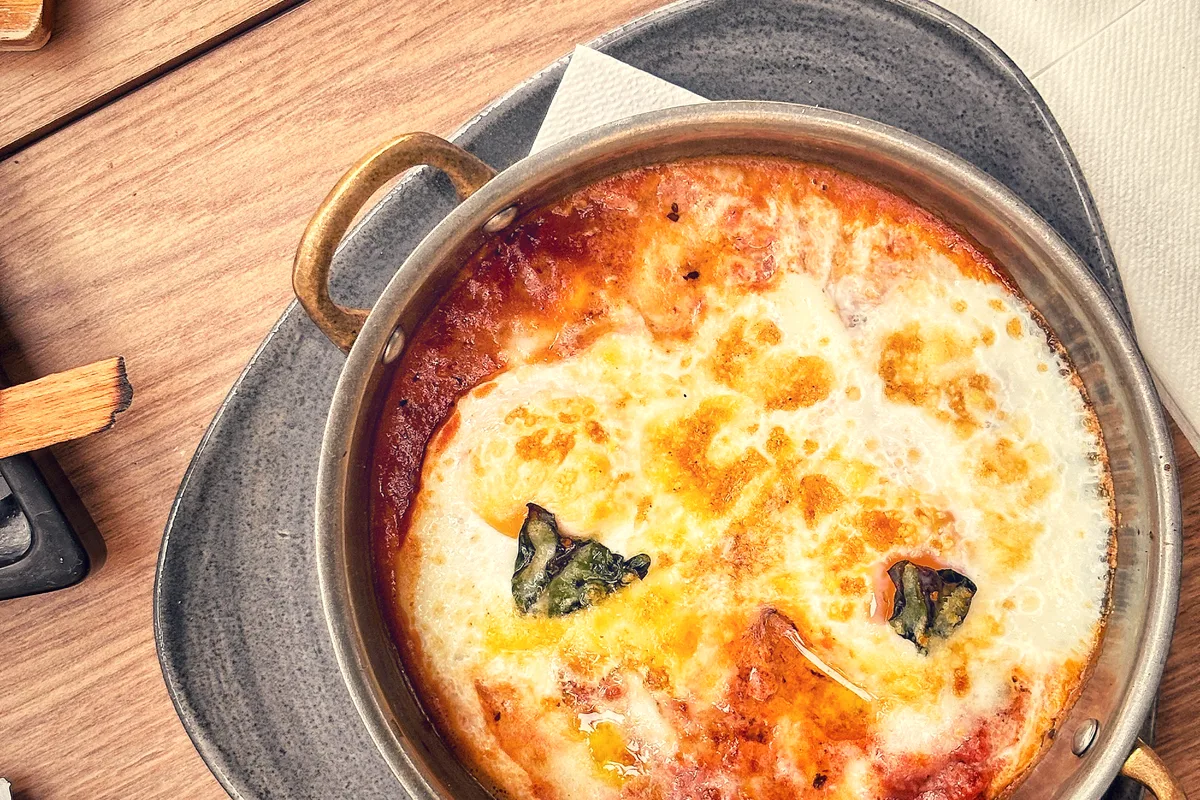 A bubbling dish of baked eggs in tomato sauce garnished with basil in a round pan