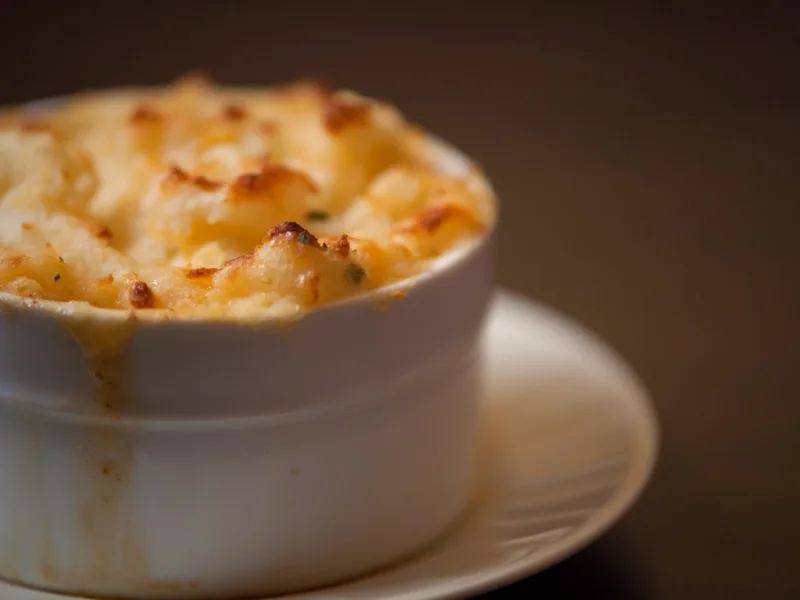 An individual shepherd's pie in a white ramekin with a golden, browned ridged mashed potato top on a small plate