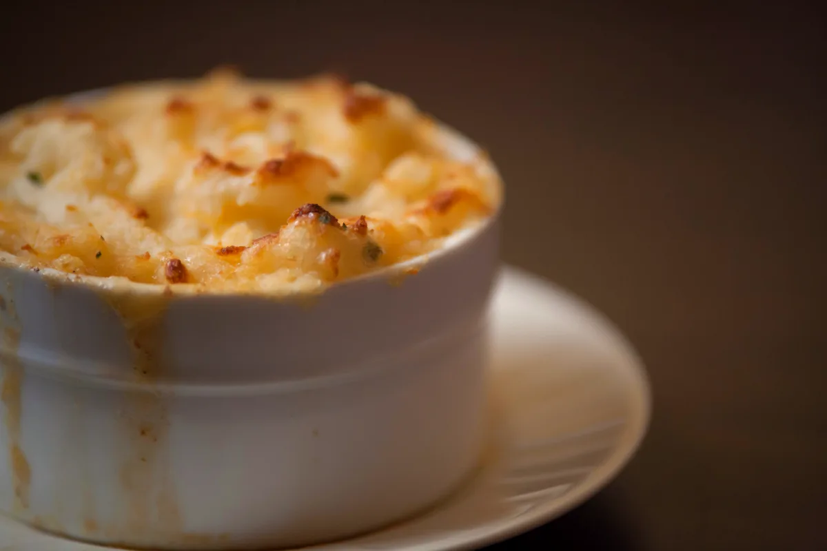 An individual shepherd's pie in a white ramekin with a golden, browned ridged mashed potato top on a small plate