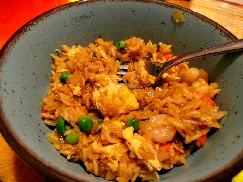Bowl of homemade shrimp fried rice with peas, diced carrots, onion, ribbons of egg and pink shrimp