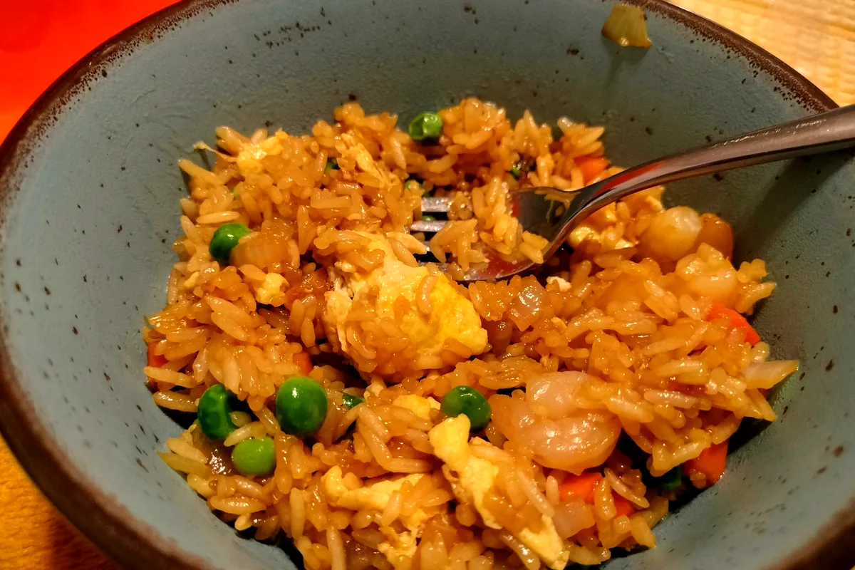 Bowl of homemade shrimp fried rice with peas, diced carrots, onion, ribbons of egg and pink shrimp