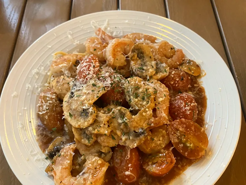 A white plate of shrimp with mushrooms and cherry tomatoes in a savory sauce, topped with grated cheese and herbs