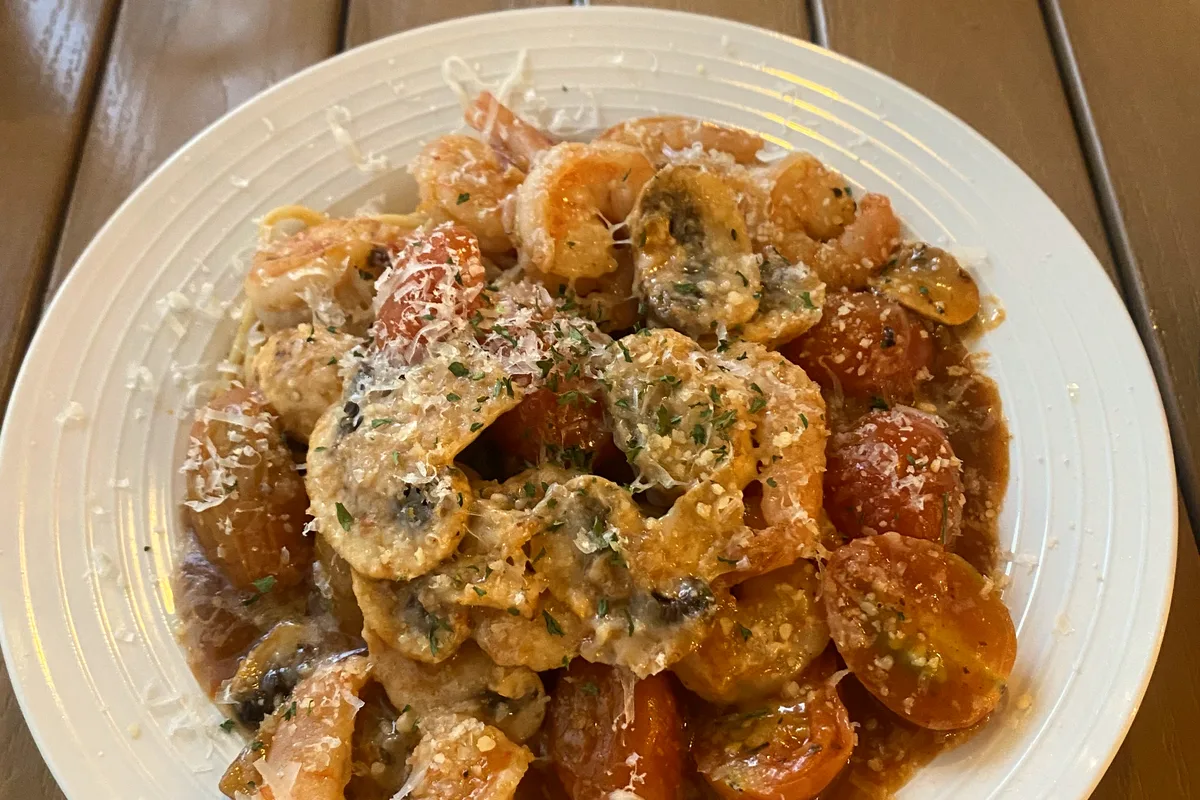 A white plate of shrimp with mushrooms and cherry tomatoes in a savory sauce, topped with grated cheese and herbs