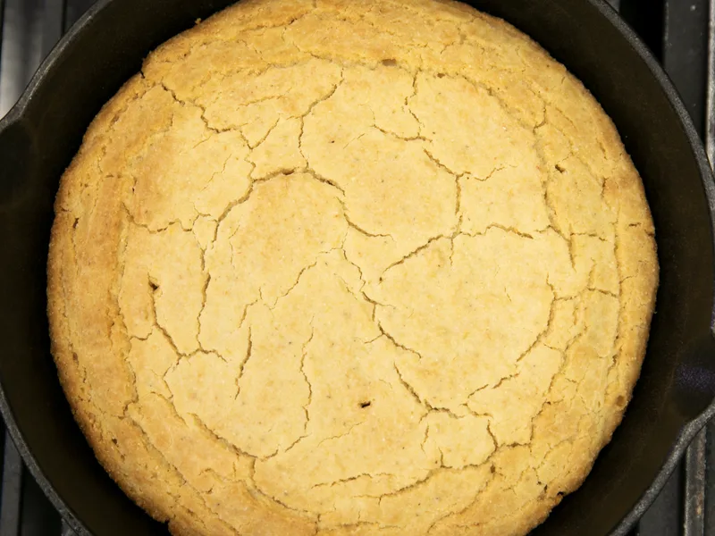 A golden skillet cornbread with a cracked top baked in a cast iron skillet