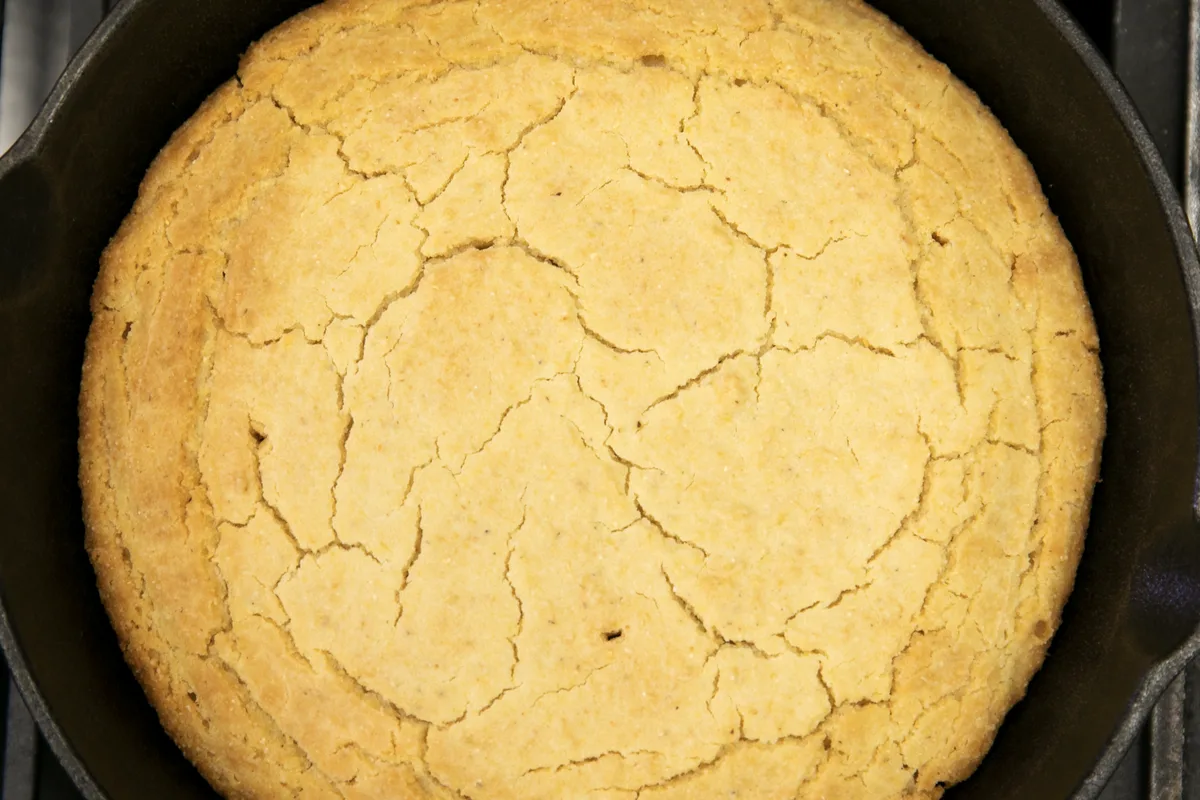 A golden skillet cornbread with a cracked top baked in a cast iron skillet