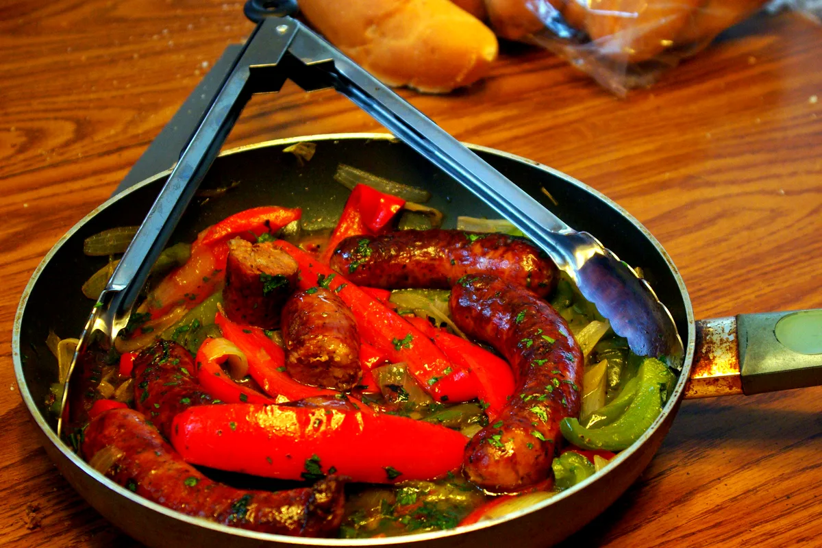 Skillet of browned Italian sausages with sliced red and green peppers and onions, scattered with fresh parsley