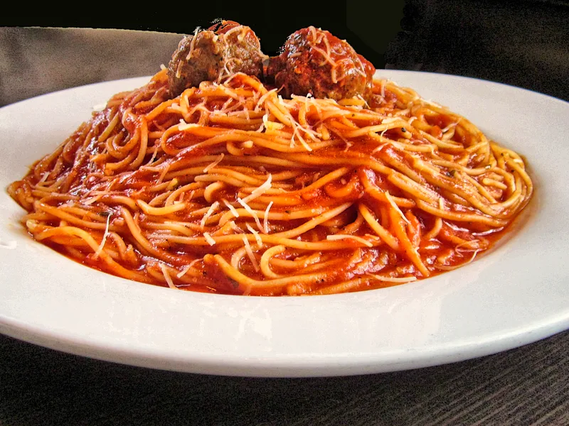 Spaghetti in tomato sauce topped with two meatballs and grated Parmesan on a white plate