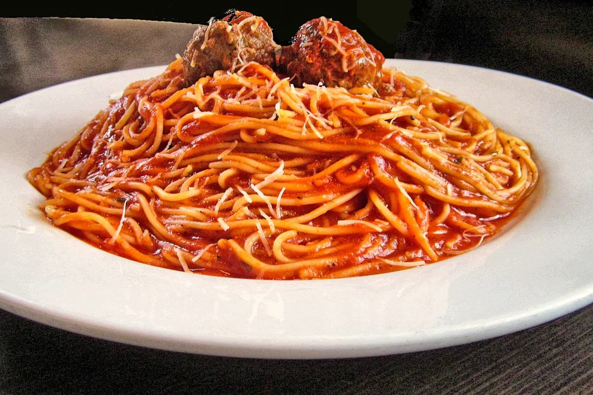 Spaghetti in tomato sauce topped with two meatballs and grated Parmesan on a white plate