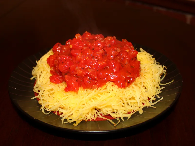 Spaghetti squash strands topped with chunky red marinara on a dark plate