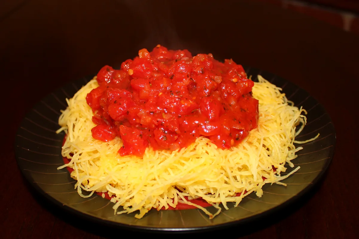 Spaghetti squash strands topped with chunky red marinara on a dark plate