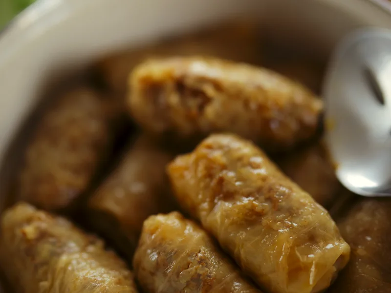 Stuffed cabbage rolls nestled in a pot under tomato sauce with a serving spoon beside them
