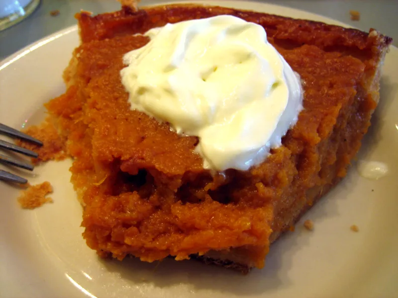A slice of classic sweet potato pie topped with a swirl of whipped cream on a white plate